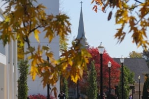 Students walk on Walsh University's campus in the fall with a steeple topped with a cross in the background.