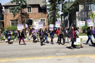 Demonstrators supporting the University of Michigan graduate student workers' strike cross a street, holding signs.