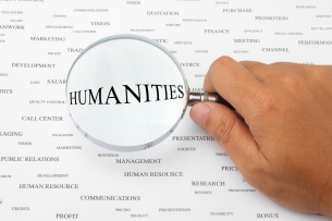 A close-up of a human hand holding a magnifying glass over a sea of words, with the word "HUMANITIES" magnified.