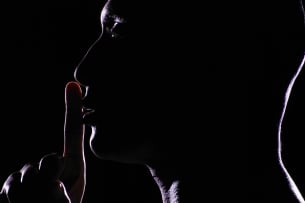 A silhouette of a person with their index finger at their lips indicating quiet.
