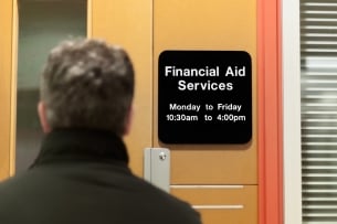 A student, photographed from behind, stands in front of the doors to the financial aid services office.