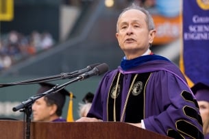 A photo of Les Wong, wearing purple academic regalia, speaking at a college event