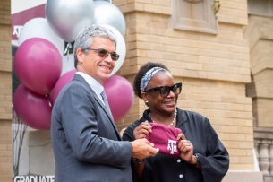 A white man and a Black woman, José Luis Bermúdez and Kathleen McElroy, together hold a Texas A&M shirt, with maroon and silver balloons behind them.