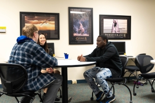 Three students meet at St. Ambrose University in a room with motivational posters hanging on the back wall.